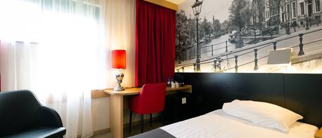 A hotel room with a bed, a desk, a chair, a lamp, and a large window with curtains.