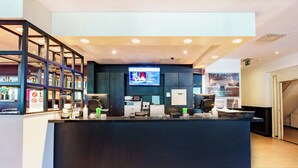 A reception desk with a digital screen, a coffee machine, and a trash bin. - Bastion Hotel Rotterdam Zuid (Rotterdam)
