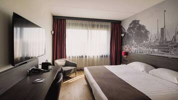 A hotel room with a bed, a desk with a chair, a television, and a large window with curtains.