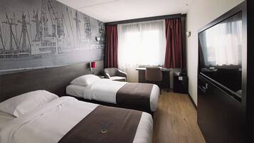 Een hotelkamer met twee bedden, een bureau, een stoel, een televisie en een muurschildering van schepen.