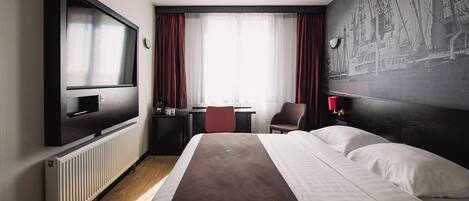 A hotel room with a large bed, a desk with a chair, a television, and a mural on the wall.