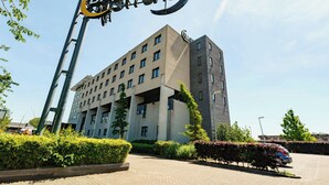 A multi-story building with a prominent sign, a parking area, and well-maintained landscaping. - Bastion Hotel Rotterdam Zuid (Rotterdam)