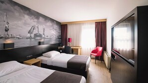 A hotel room with two beds, a desk, a chair, a TV, and a large window with curtains. - Bastion Hotel Rotterdam Zuid (Rotterdam)