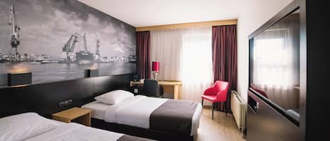 A hotel room with two beds, a desk, a chair, a TV, and a large window with curtains.