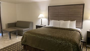 A hotel room with a bed, a sofa, a nightstand, and a lamp.