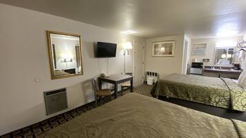 A hotel room with two beds, a desk with a chair, a television, a mirror, and a small kitchenette.