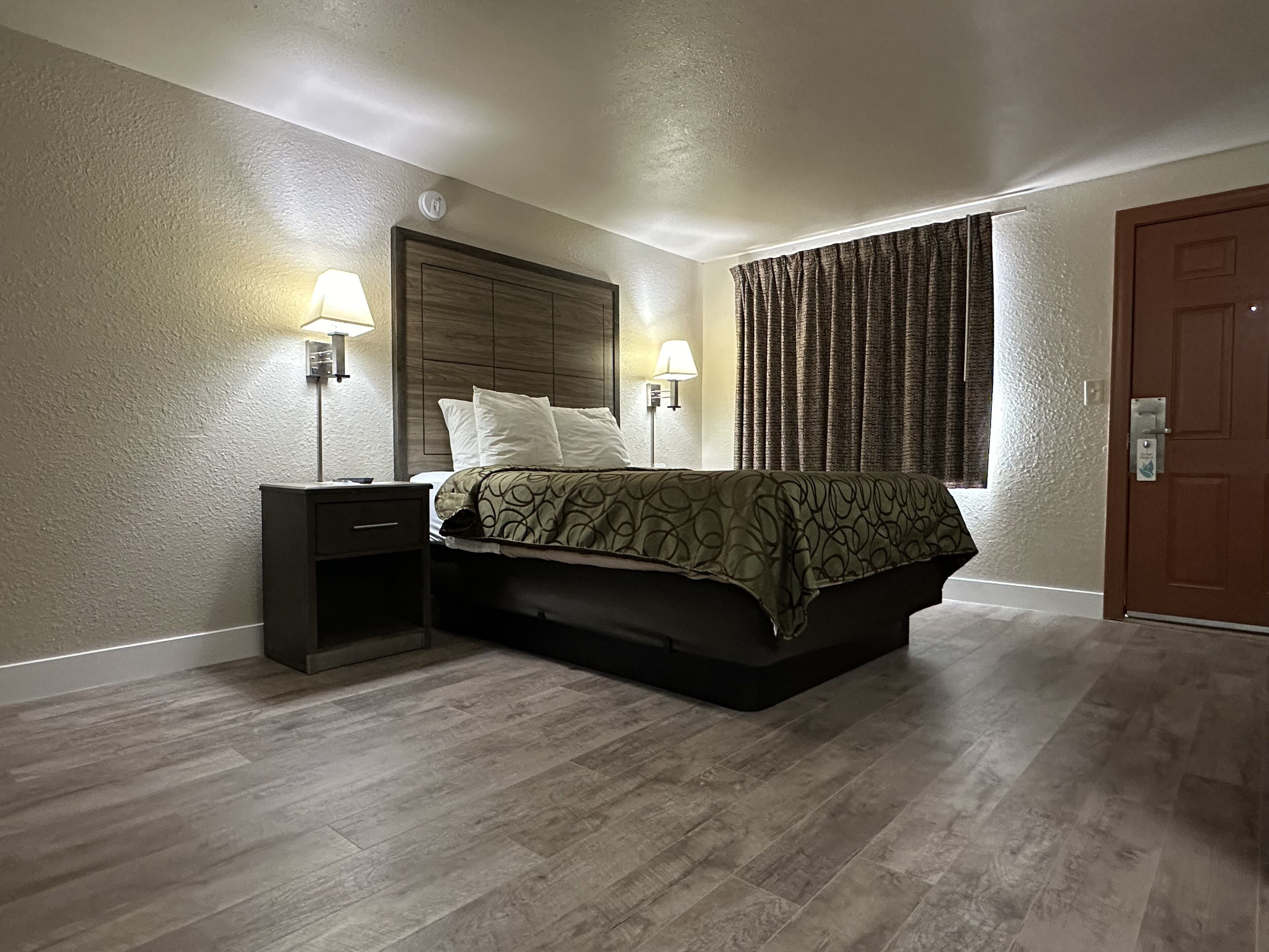 Een slaapkamer met een bed, twee nachtkastjes, een raam met gordijnen en een deur.