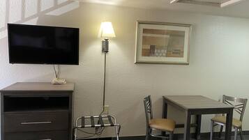 Een hotelkamer met een flatscreen televisie, een bureau, een stoel, een lamp en een ingelijst kunstwerk aan de muur.
