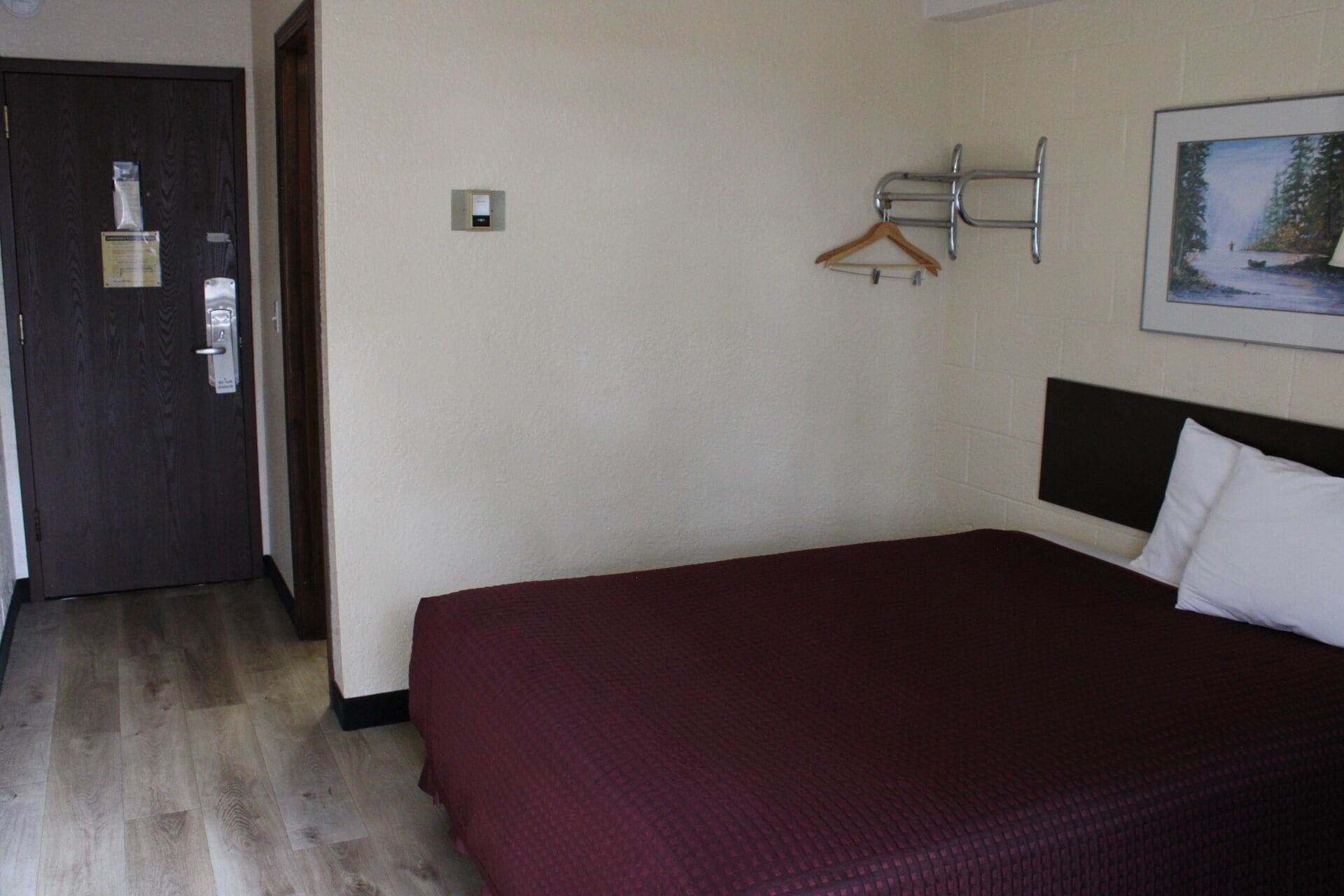 Une chambre d’hôtel avec un lit, une porte à clé, un porte-manteau et un tableau accroché au mur.