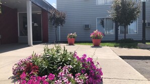 A building with a covered entrance, potted plants, and a flower bed with various flowers. - Aero Inn (Kalispell)