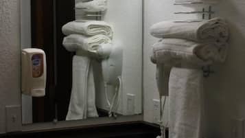Un baño con lavamanos, espejo y toallas apiladas en un perchero.
