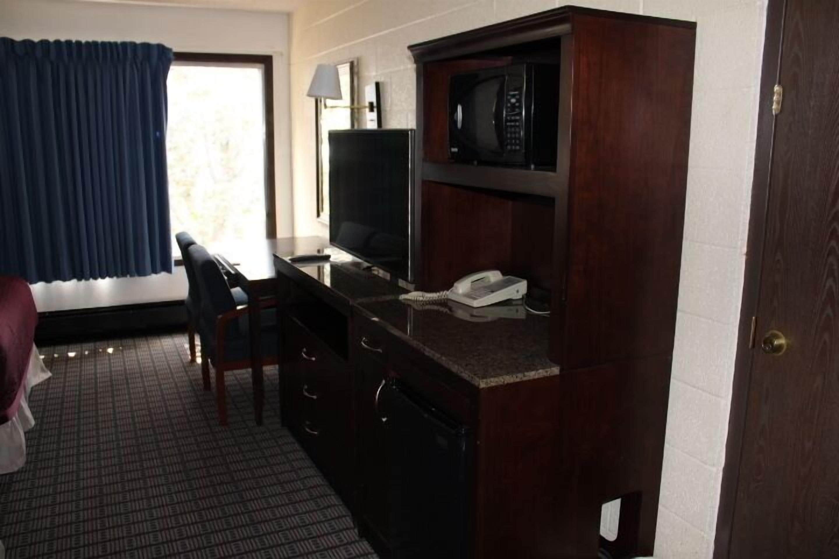Habitación de hotel con escritorio de madera oscura, televisor, teléfono y ventana con cortinas azules.