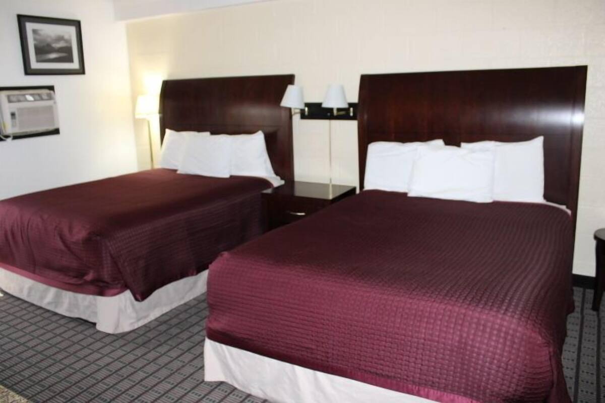 Ein Hotelzimmer mit zwei Doppelbetten, die dunklen Holz Kopfteile und weiße Bettwäsche haben.