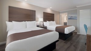Hotellihuone, jossa on kaksi sänkyä, yöpöytä lampun kanssa, seinälle kiinnitetty kello ja ovi, joka johtaa kylpyhuoneeseen.