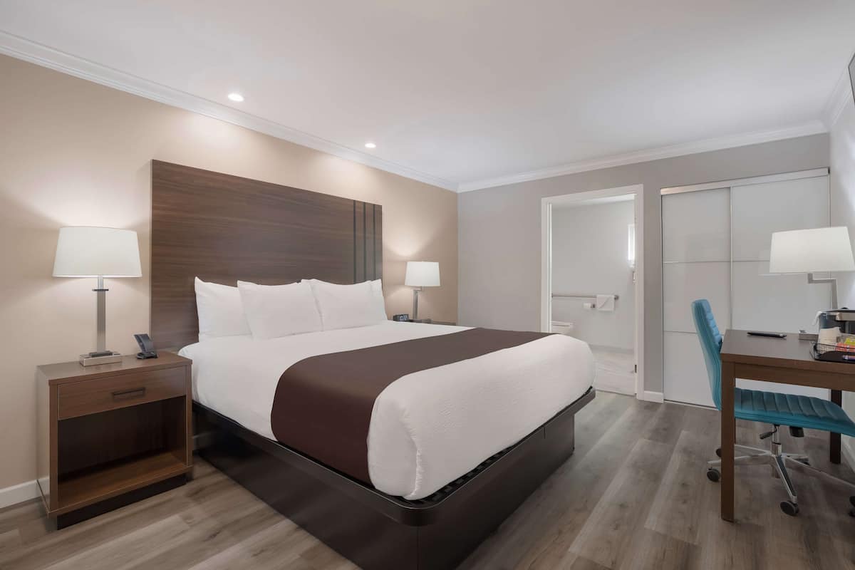 Una habitación de hotel moderna con una cama grande, mesitas de noche con lámparas, un escritorio con silla y un armario.