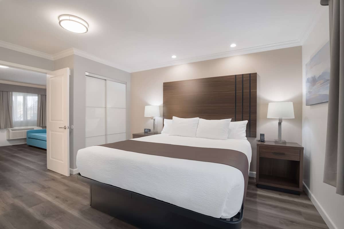 Habitación de hotel moderna con una cama grande, lámparas de noche, un cabecero de madera y vistas al pasillo.