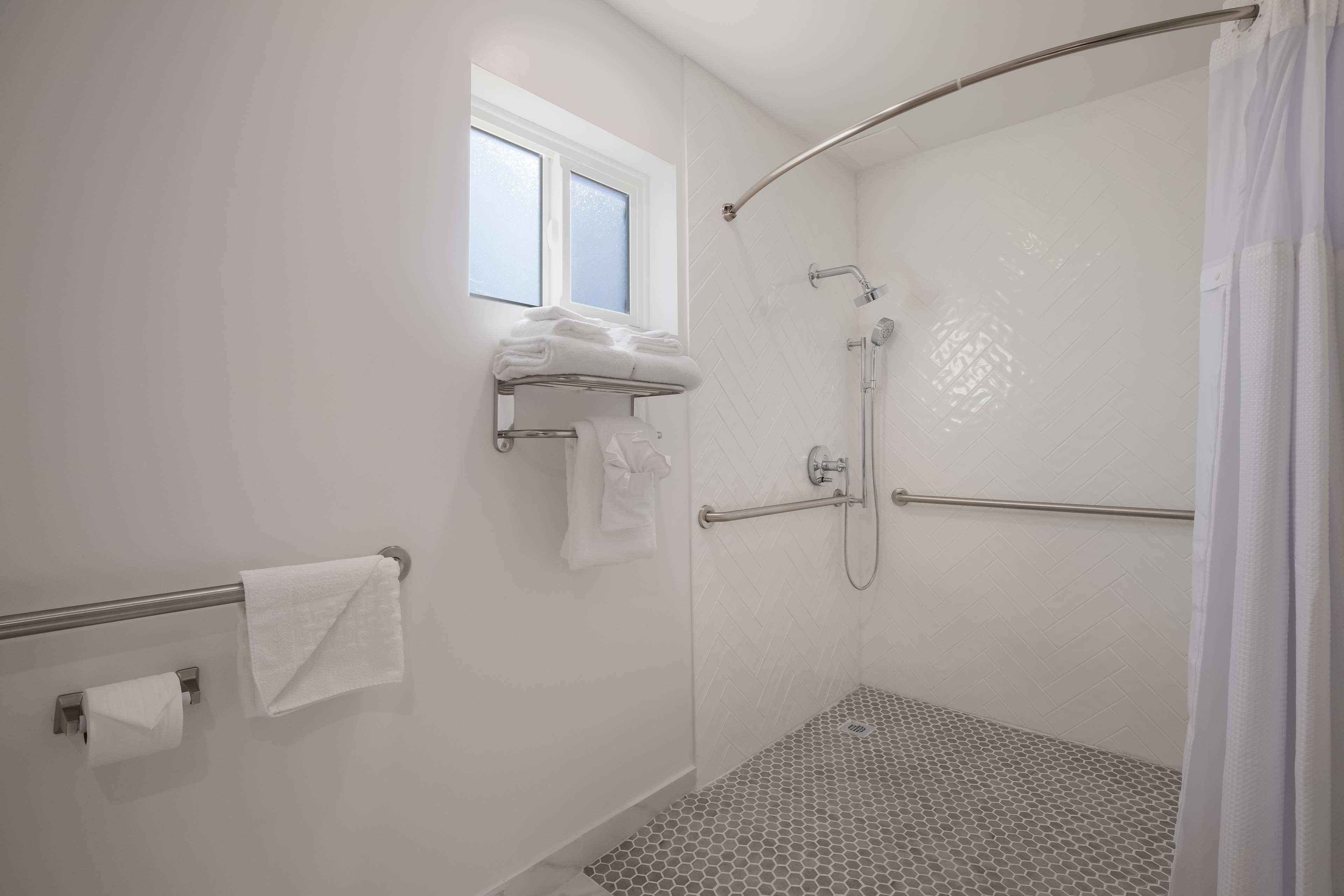 Een moderne douchecel met een glazen deur, een handdoekhouder met opgevouwen handdoeken en een raam boven de douche.