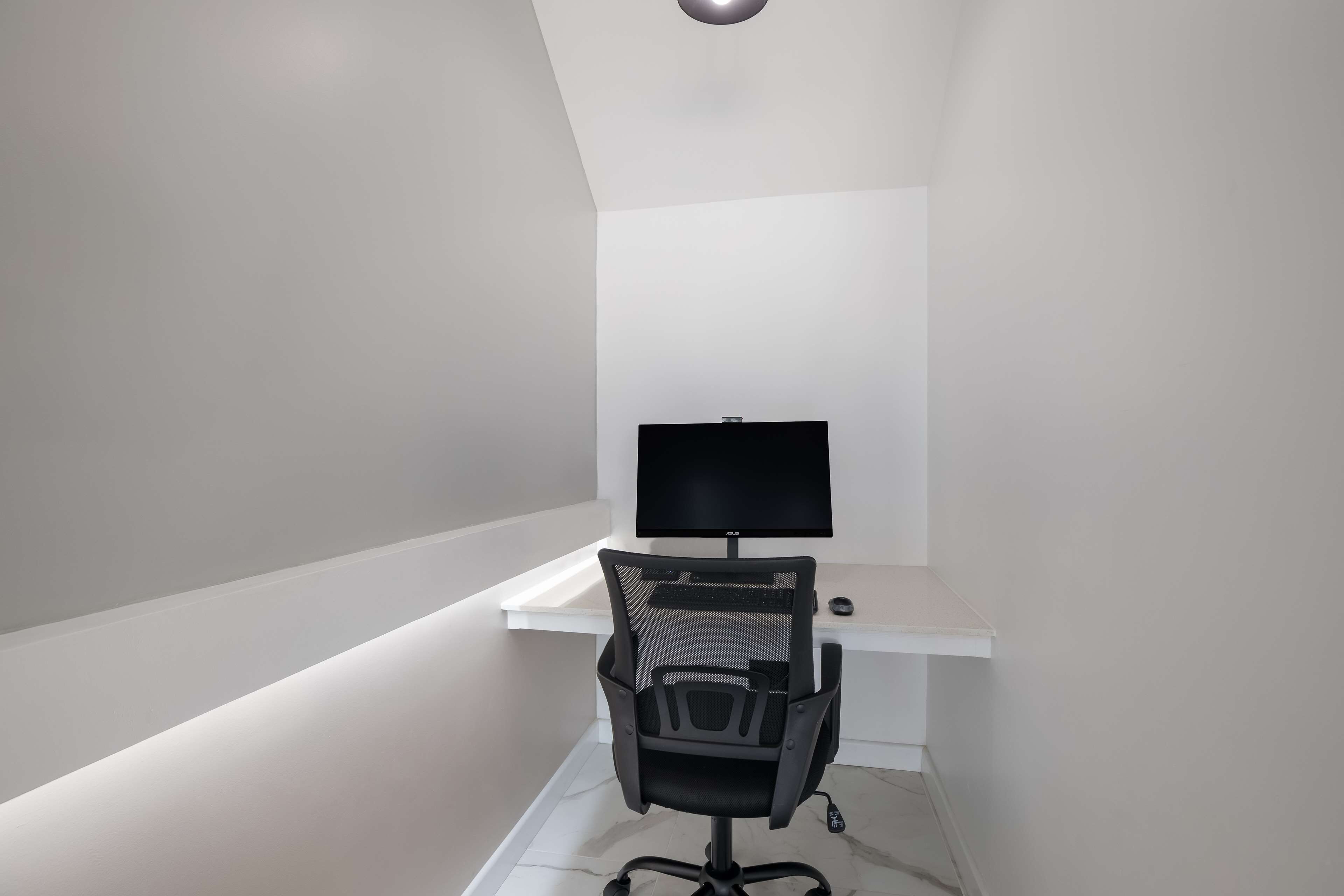 A modern, minimalistic office space with a white desk, black office chair, and a flat-screen monitor.