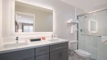 Un baño moderno con un espejo grande, dos lavamanos, un inodoro y una ducha con cerramiento de vidrio.