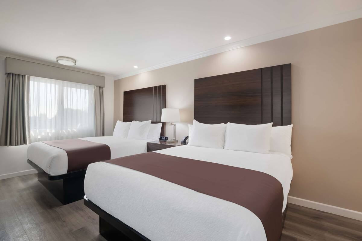 Una habitación de hotel con dos camas, una mesita de noche con lámpara y una ventana con cortinas.