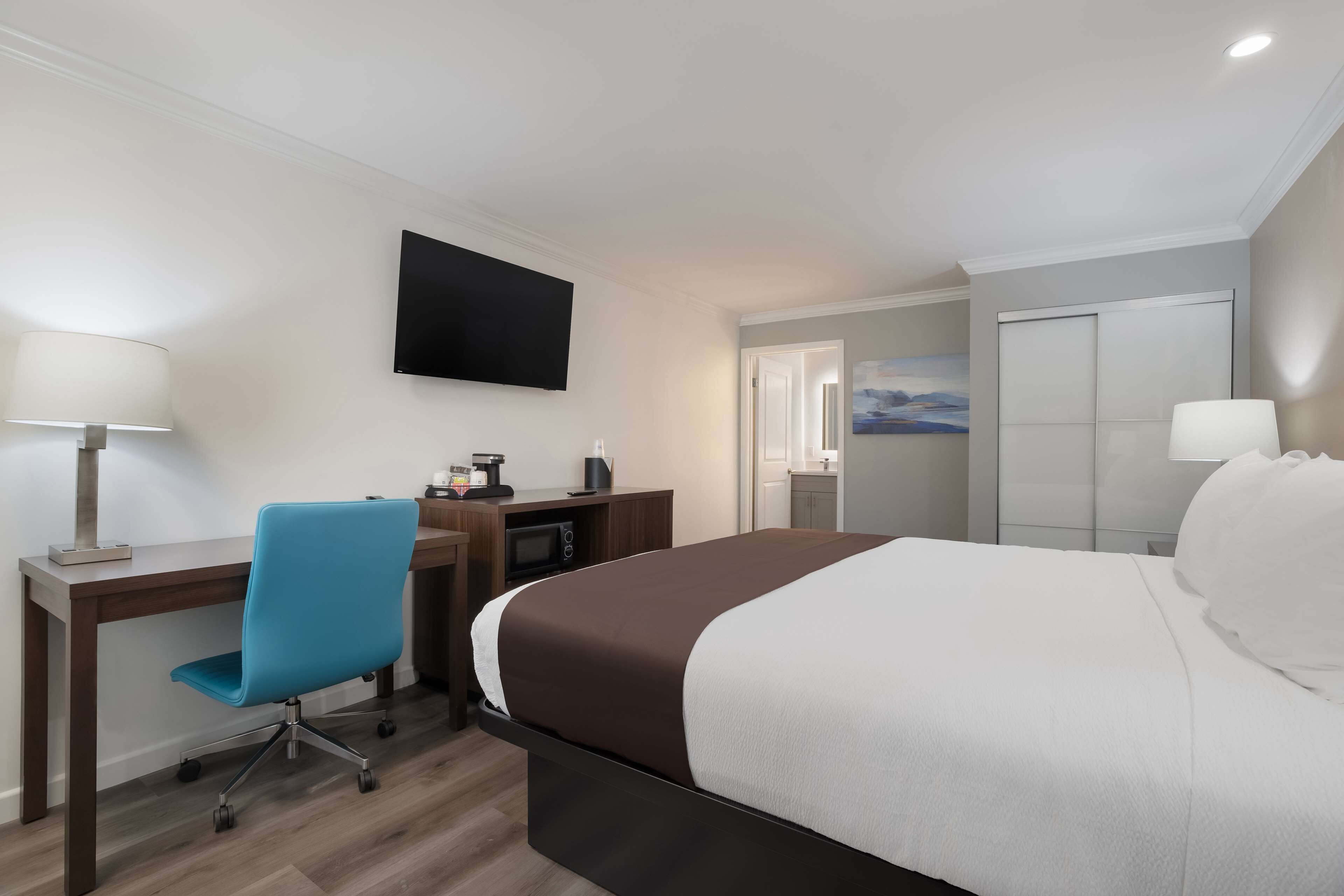 A hotel room with a bed, desk, chair, TV, and a painting on the wall.