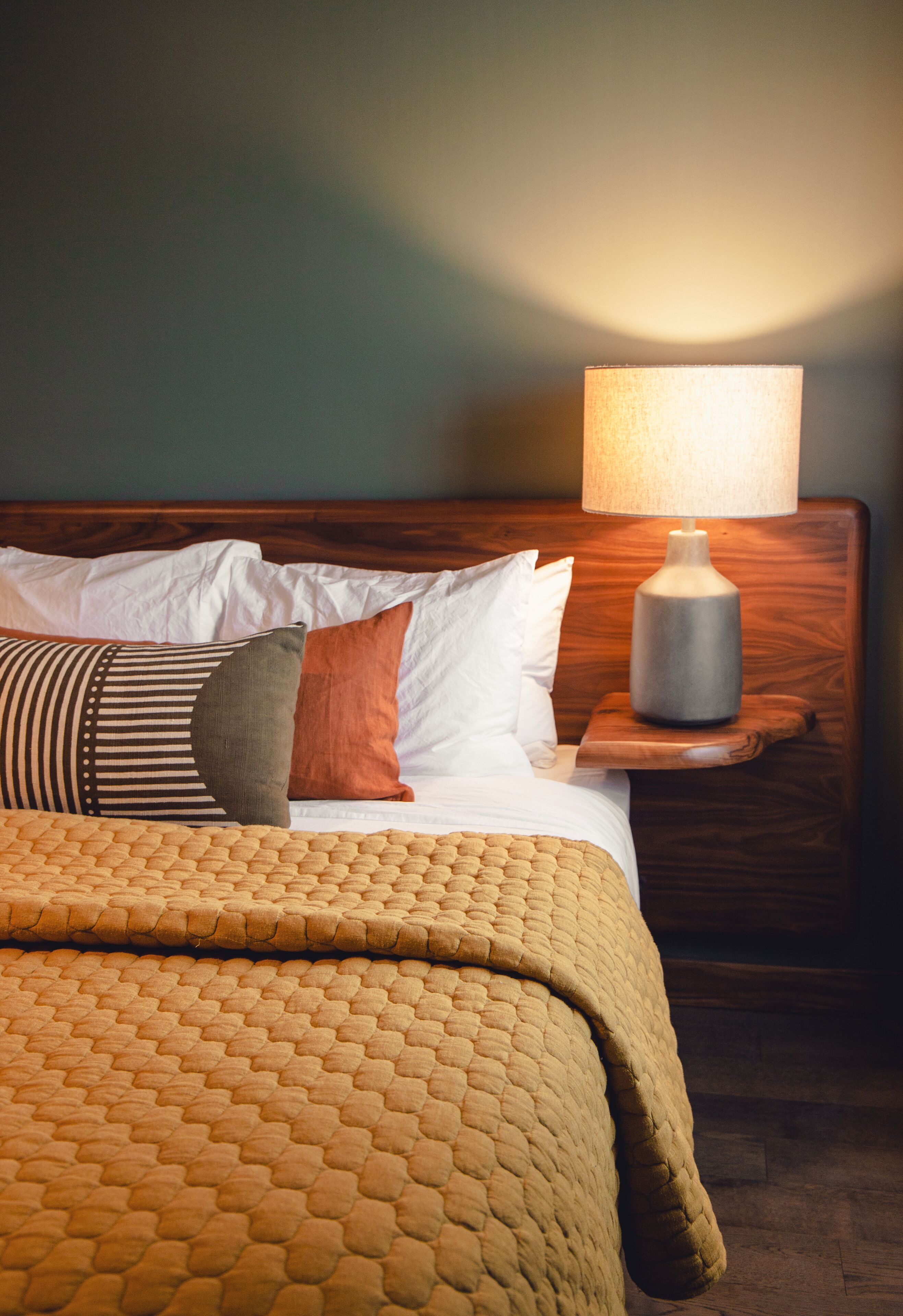 A neatly made bed with a patterned blanket, a wooden headboard, and a bedside table with a lamp.