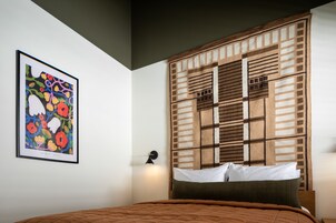 A bedroom with a bed, a wall-mounted light, and a framed floral artwork.