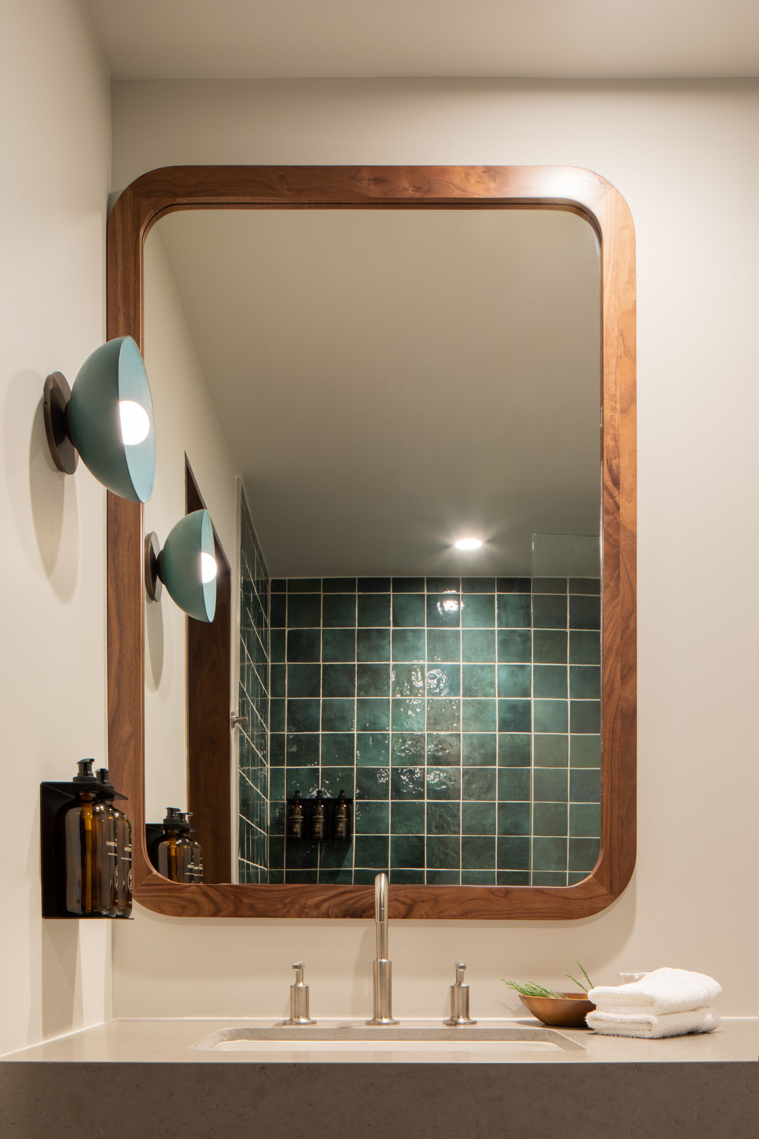A bathroom with a wooden-framed mirror, a sink with two faucets, and a wall-mounted light fixture.