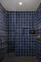 Eine Dusche mit blauen Fliesen, einer Handbrause und einem fest installierten Bedienfeld.