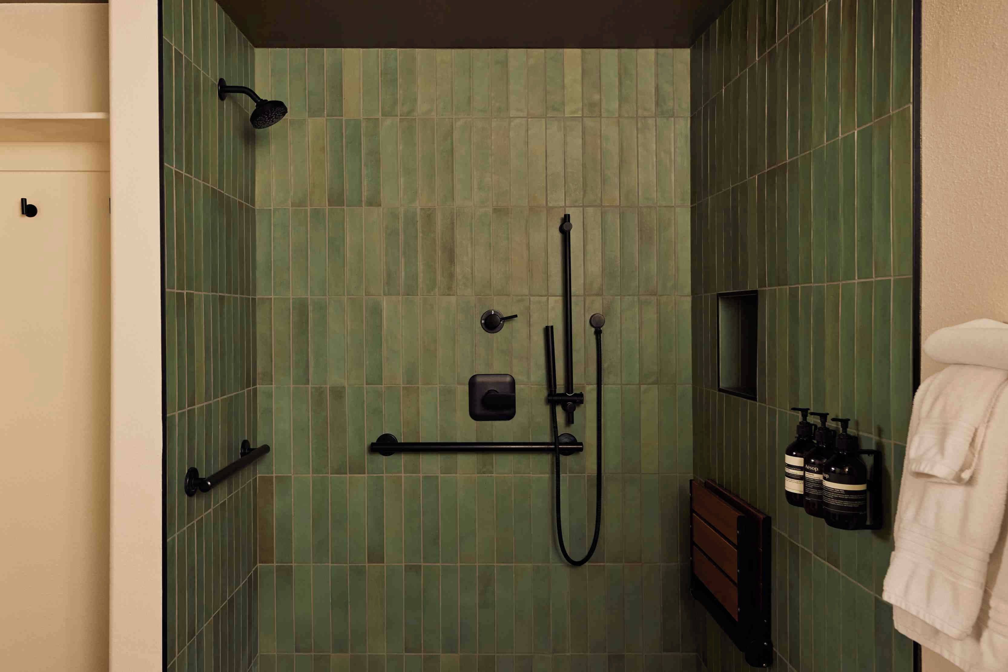 A bathroom with green tiled walls, a shower, a towel rack, and a bottle of lotion.