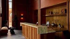 A reception area with a wooden reception desk, a potted plant, and a wall-mounted shelf with decorative items. - Hotel Marina Riviera (Big Bear Lake)