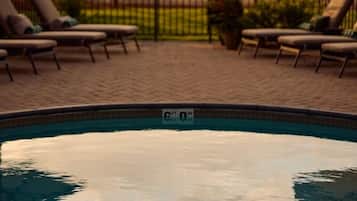 Piscina con sillas de descanso y sombrillas, rodeada por una cerca y con vistas a montañas.