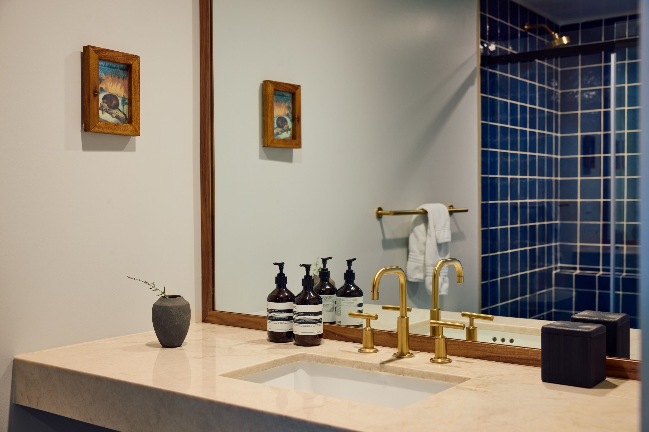 A bathroom with a sink, golden faucets, a mirror, and a blue-tiled shower area.