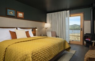 Een hotelkamer met een groot bed, een nachtkastje met een lamp, een stoel, uitzicht op de omgeving via een schuifdeur en een open haard.
