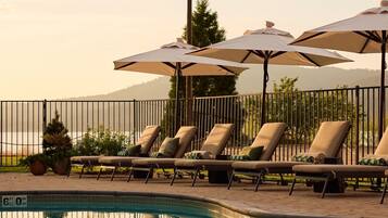 A poolside area with lounge chairs and umbrellas, a clear view of the water, and a mountain in the background.