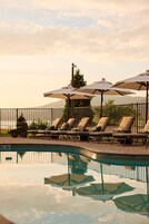 A poolside area with lounge chairs and umbrellas, a clear view of the water, and a mountain in the background.