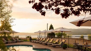 A poolside area with lounge chairs and umbrellas, a pool, and a view of a body of water and hills. - Hotel Marina Riviera (Big Bear Lake)