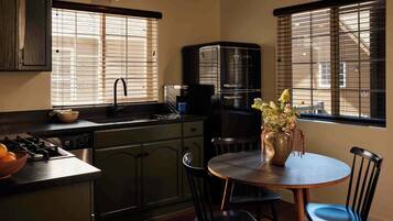 A kitchen with a stove, sink, and a coffee maker. There is a dining table with chairs and a vase with flowers.