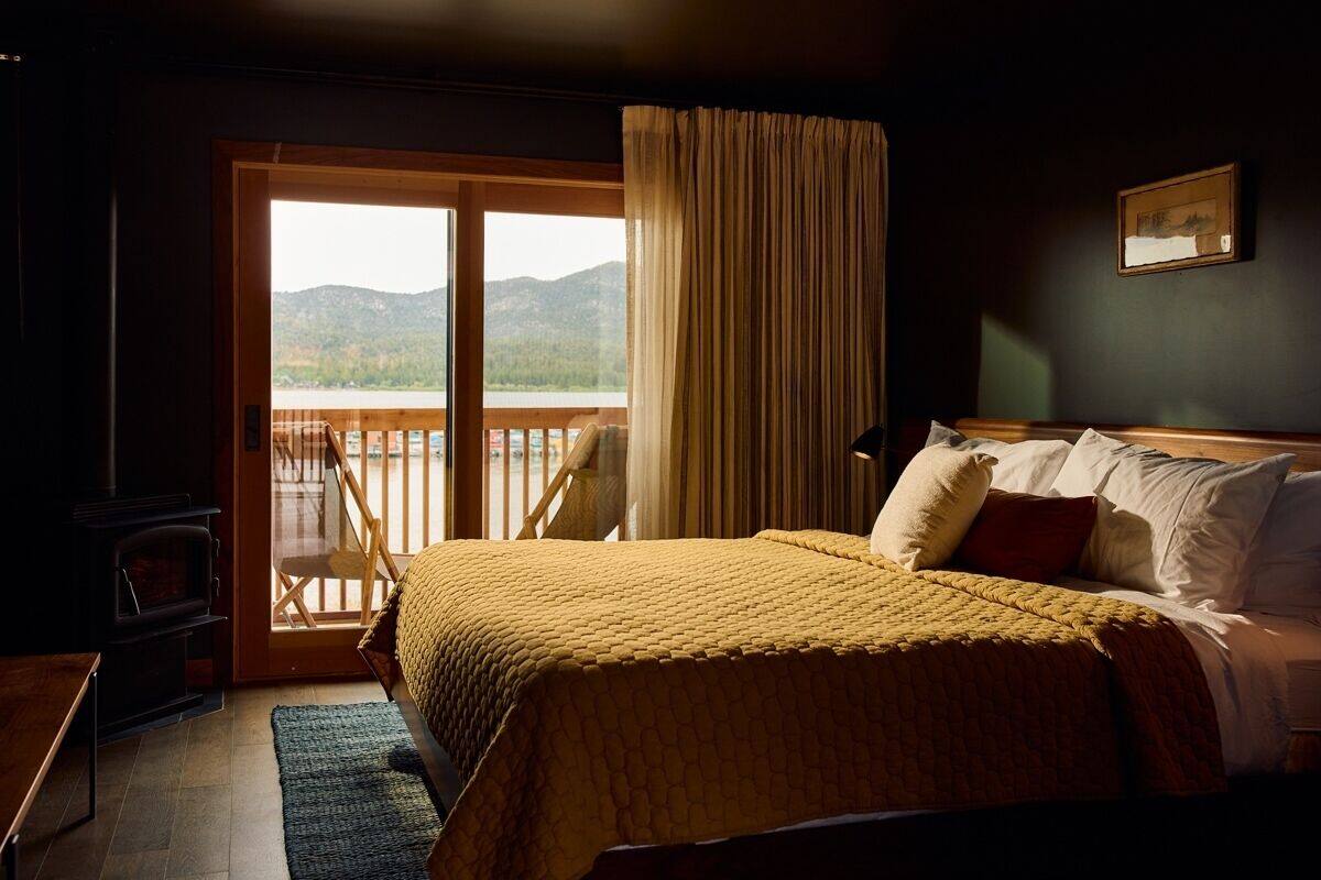A bedroom with a bed, a wooden desk, a fireplace, and a balcony with a view of mountains.