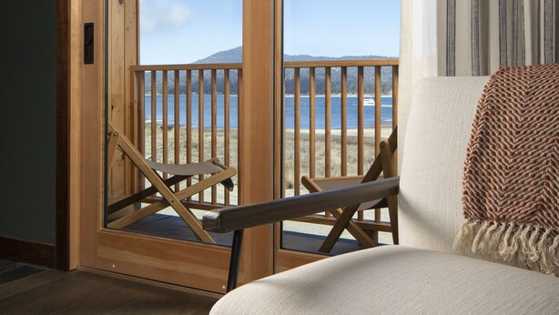 A room with a wooden door leading to a balcony with a view of a lake and mountains. - Hotel Marina Riviera (Big Bear Lake)