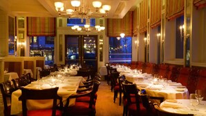 A restaurant with multiple tables set for dining, large windows with curtains, and a chandelier. - New Sheridan Hotel (Telluride)