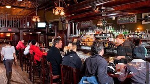 A bar with wooden decor, a counter with a bartender, and patrons seated at tables. - New Sheridan Hotel (Telluride)