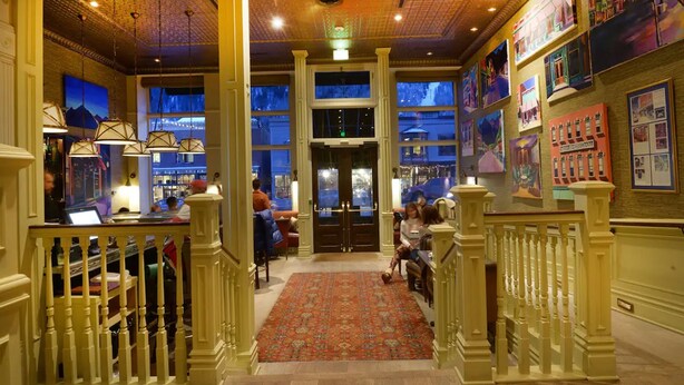 A lobby with a patterned carpet, wooden railings, and artwork on the walls. - New Sheridan Hotel (Telluride)