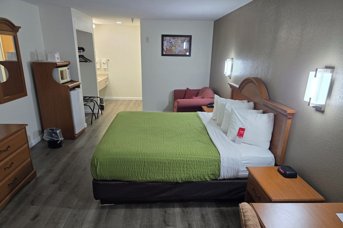 Une chambre d’hôtel avec un lit, une tête de lit en bois, une table de chevet et un petit bureau.