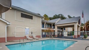 A swimming pool with lounge chairs and a lifeguard stand, surrounded by a building with a flag and a 'No Diving' sign.