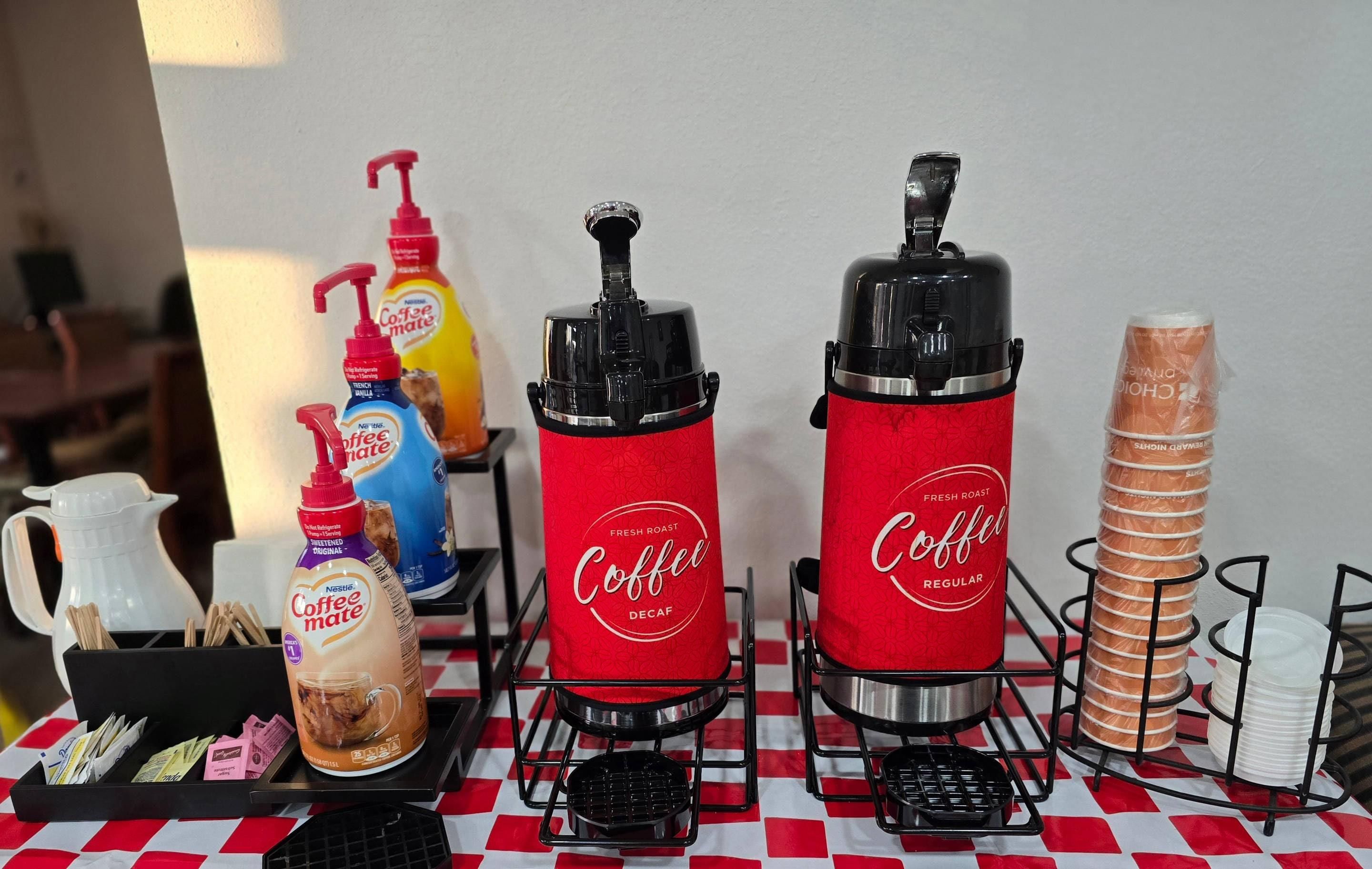A coffee station with two coffee dispensers, a coffee maker, and a stack of bread.