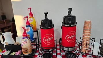 A coffee station with two coffee dispensers, a coffee maker, and a stack of bread.