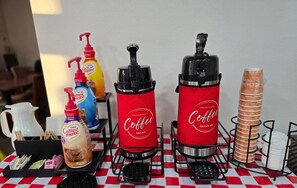 A coffee station with two coffee dispensers, a coffee maker, and a stack of bread. - Econo Lodge Villa Rica (Villa Rica)