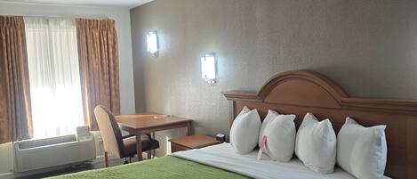 A hotel room with a bed, a desk, a chair, and a window with curtains.