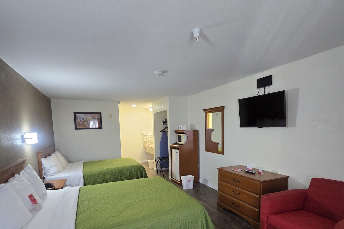 Une chambre d’hôtel avec deux lits simples, un canapé rouge, une commode en bois, un téléviseur fixé au mur et un petit bureau avec une chaise.